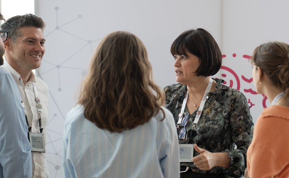 Three women smiling and networking with two male researchers/medical professionals at an event